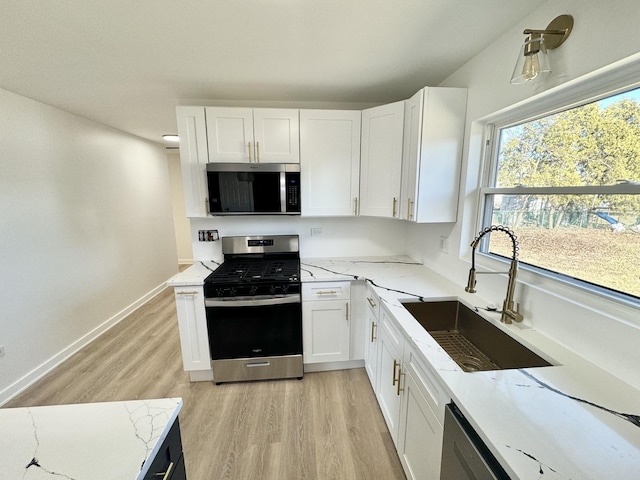 kitchen featuring stainless steel appliances, white cabinetry, light stone countertops, and sink