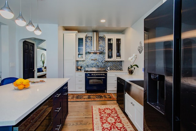 kitchen featuring a center island, wall chimney range hood, white cabinets, and black appliances