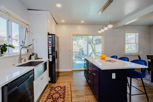 kitchen featuring a breakfast bar area, decorative light fixtures, light hardwood / wood-style flooring, a kitchen island, and black appliances