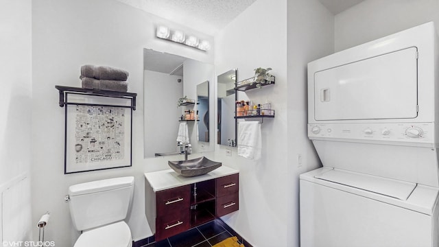 bathroom featuring stacked washing maching and dryer, vanity, toilet, tile patterned floors, and a textured ceiling