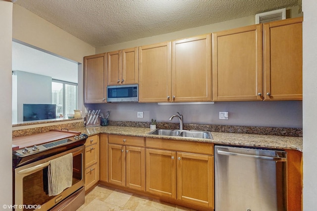 kitchen featuring light stone countertops, appliances with stainless steel finishes, sink, and a textured ceiling