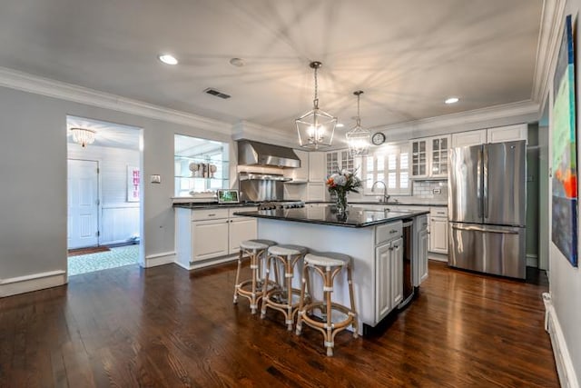 kitchen with a kitchen island, white cabinets, pendant lighting, stainless steel appliances, and wall chimney range hood