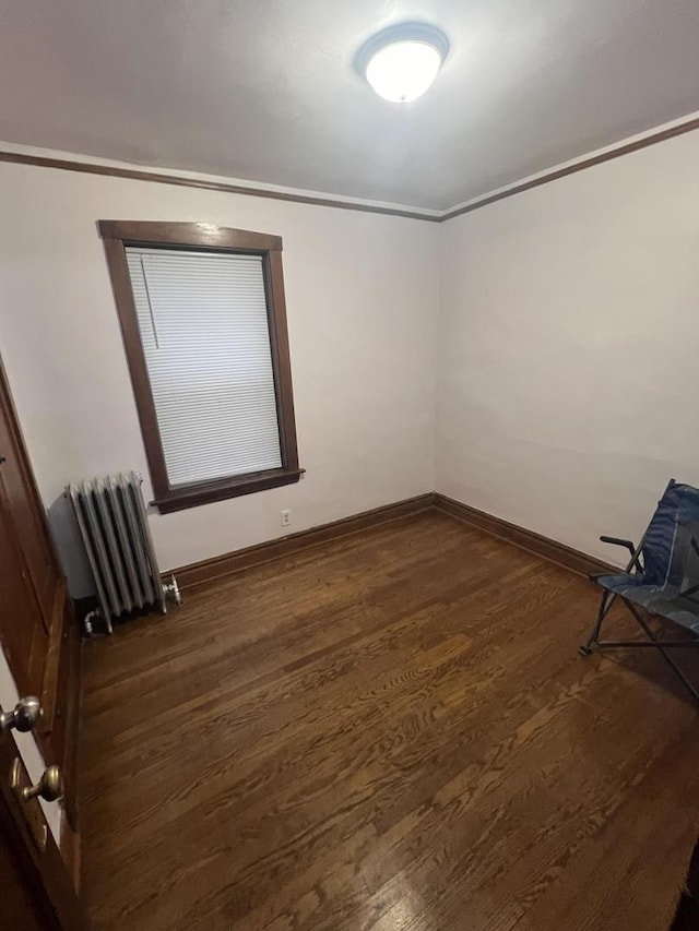 empty room with dark hardwood / wood-style flooring, radiator, and ornamental molding