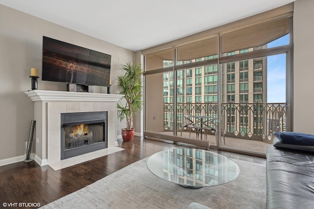 living room featuring a tiled fireplace, dark hardwood / wood-style flooring, plenty of natural light, and a wall of windows