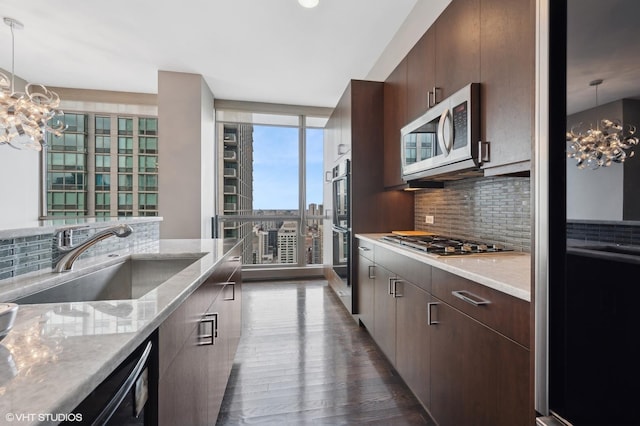 kitchen with appliances with stainless steel finishes, tasteful backsplash, sink, dark brown cabinets, and an inviting chandelier