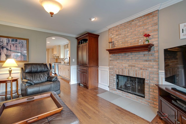 living room with ornamental molding, a brick fireplace, sink, and light hardwood / wood-style flooring