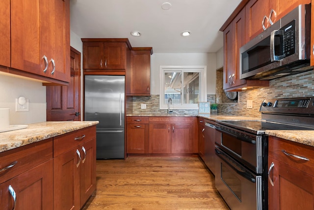 kitchen with light stone counters, stainless steel appliances, sink, and light wood-type flooring