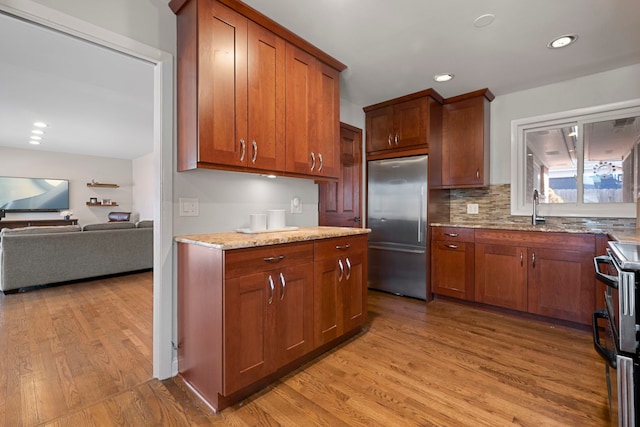 kitchen with sink, light stone counters, light hardwood / wood-style flooring, appliances with stainless steel finishes, and backsplash