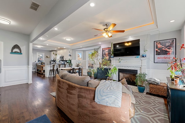 living room featuring dark hardwood / wood-style flooring, a raised ceiling, and ceiling fan