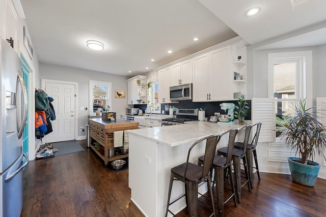 kitchen featuring a breakfast bar area, white cabinetry, appliances with stainless steel finishes, dark hardwood / wood-style floors, and kitchen peninsula