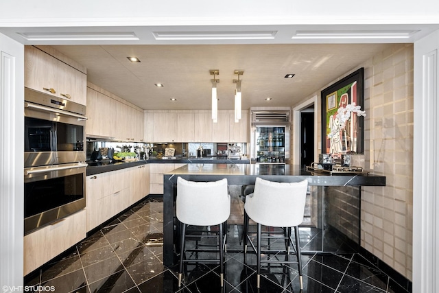 kitchen featuring stainless steel double oven, light brown cabinetry, kitchen peninsula, and a breakfast bar area