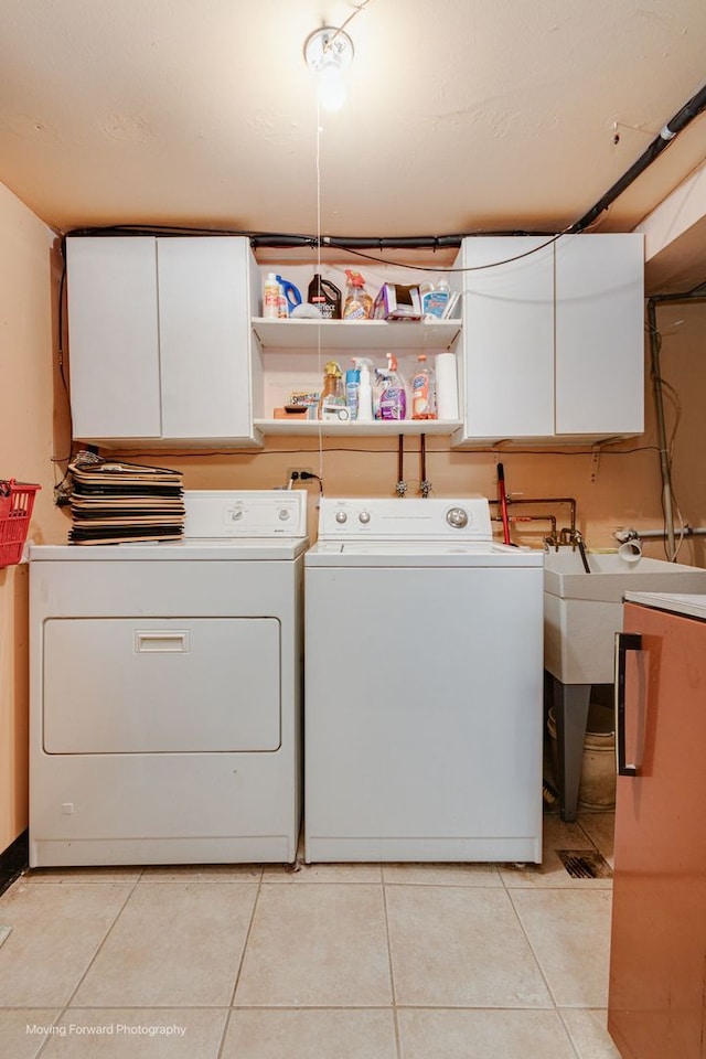 clothes washing area featuring light tile patterned flooring, cabinets, and washing machine and clothes dryer