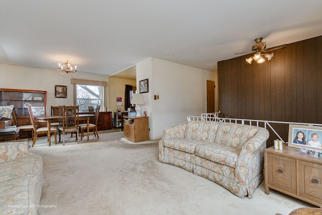 carpeted living room with ceiling fan with notable chandelier and wood walls