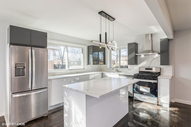 kitchen featuring wall chimney exhaust hood, sink, a center island, stainless steel appliances, and light stone countertops