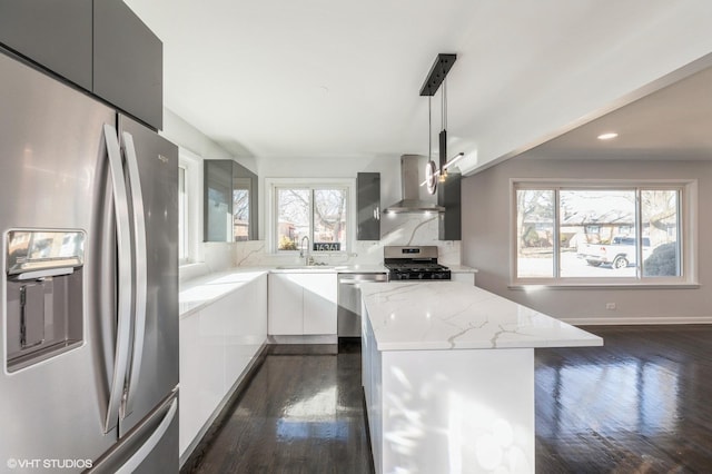 kitchen with sink, appliances with stainless steel finishes, a center island, decorative light fixtures, and wall chimney exhaust hood