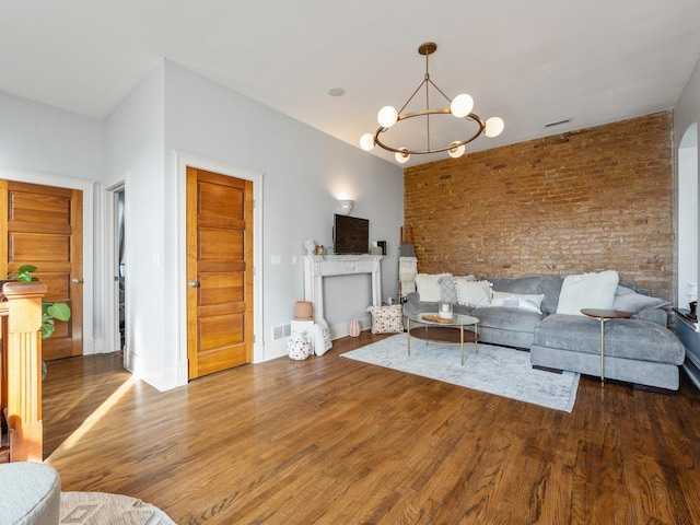 unfurnished living room with an inviting chandelier, a fireplace, wood-type flooring, and brick wall