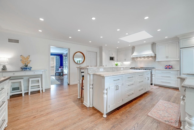 kitchen with custom exhaust hood, a center island, white cabinets, and a kitchen breakfast bar