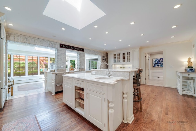 kitchen featuring white cabinetry, sink, hardwood / wood-style flooring, crown molding, and a center island with sink