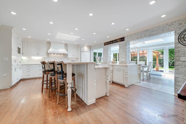 kitchen with custom exhaust hood, a kitchen island, a kitchen bar, and kitchen peninsula