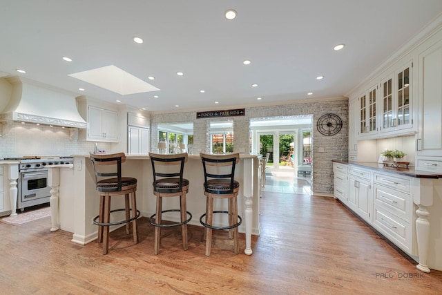 kitchen with white cabinetry, ornamental molding, luxury range, and premium range hood