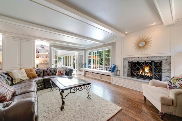 living room featuring beam ceiling, wood-type flooring, ornamental molding, and a high end fireplace