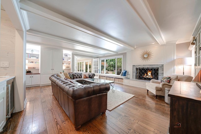 living room featuring wood-type flooring, a premium fireplace, and beamed ceiling