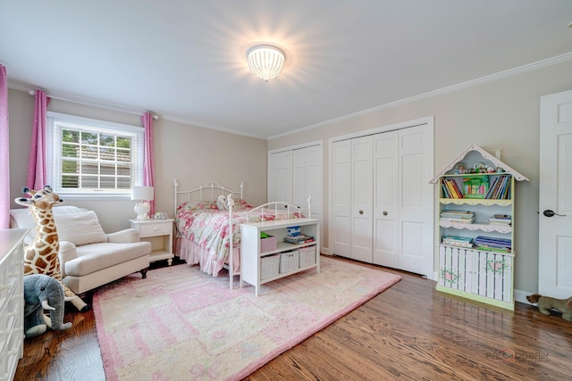 bedroom with hardwood / wood-style flooring, ornamental molding, and two closets