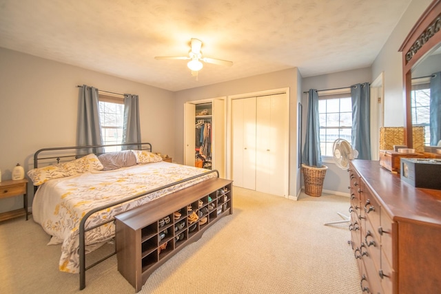 bedroom with multiple closets, light colored carpet, and ceiling fan