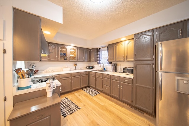 kitchen with sink, appliances with stainless steel finishes, light hardwood / wood-style floors, a textured ceiling, and wall chimney exhaust hood