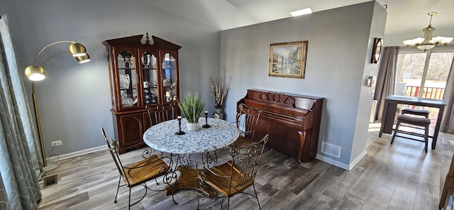 dining space featuring a notable chandelier, visible vents, lofted ceiling, and wood finished floors