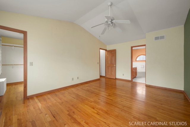 unfurnished bedroom with ensuite bathroom, a spacious closet, vaulted ceiling, and light wood-type flooring