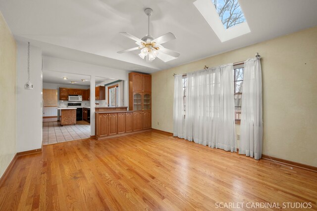 unfurnished living room featuring light hardwood / wood-style flooring, lofted ceiling with skylight, and ceiling fan