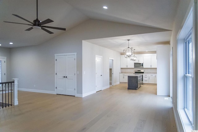 unfurnished living room with lofted ceiling, ceiling fan with notable chandelier, and light wood-type flooring