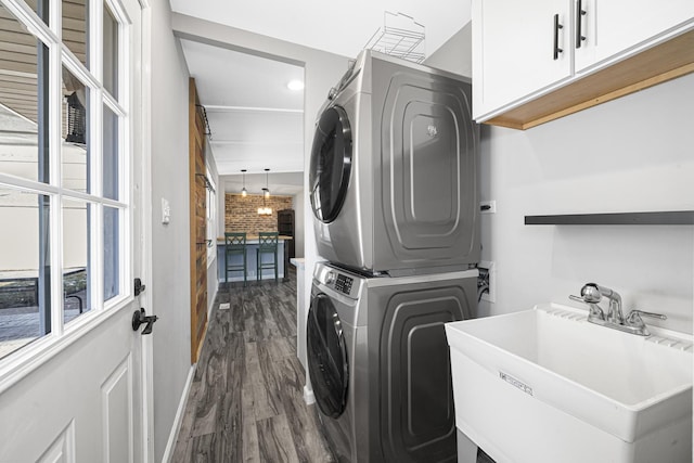 laundry room with sink, dark wood-type flooring, cabinets, and stacked washer and clothes dryer