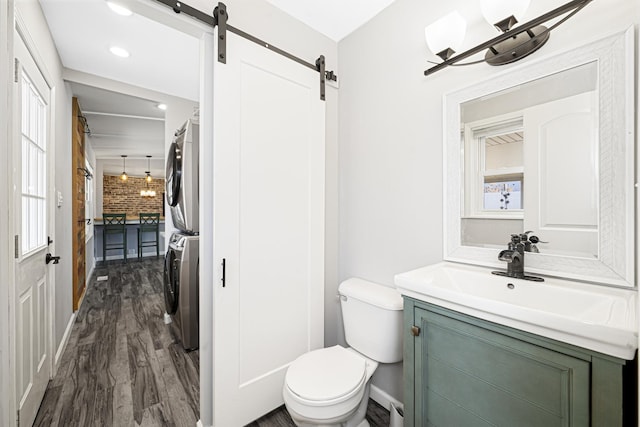 bathroom with hardwood / wood-style flooring, stacked washer and dryer, vanity, and toilet