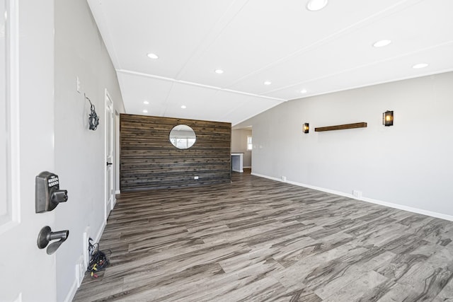 unfurnished living room featuring wood-type flooring, lofted ceiling, and wooden walls