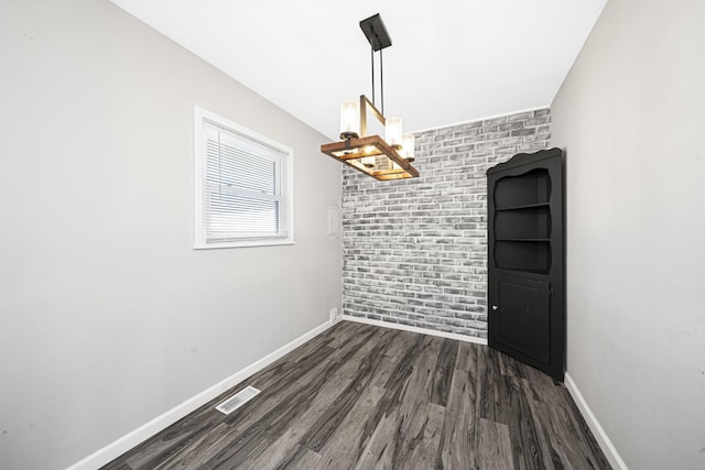 unfurnished dining area with dark wood-type flooring and brick wall