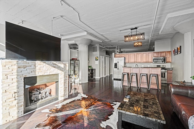 living room featuring dark hardwood / wood-style flooring, a stone fireplace, and ornate columns