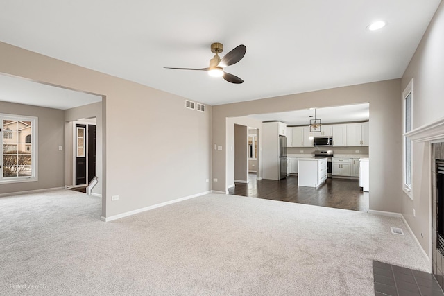 unfurnished living room with a tile fireplace, ceiling fan, and dark carpet