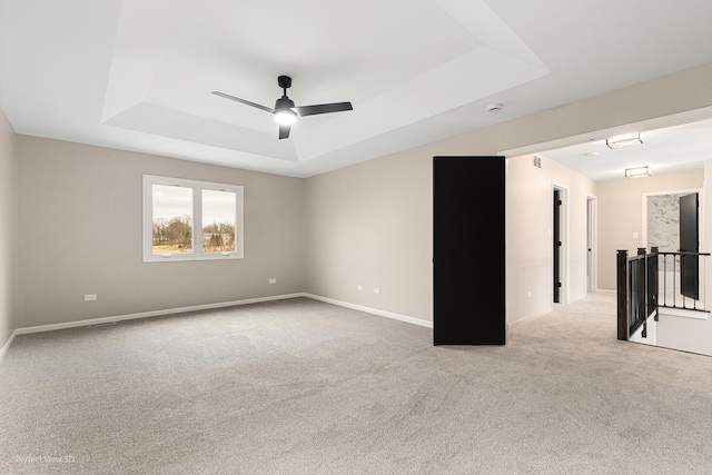 empty room with light colored carpet, a raised ceiling, and ceiling fan