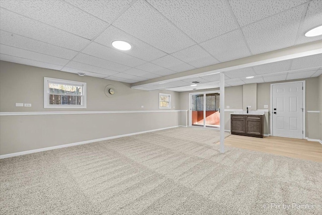 basement featuring a paneled ceiling, plenty of natural light, sink, and light carpet