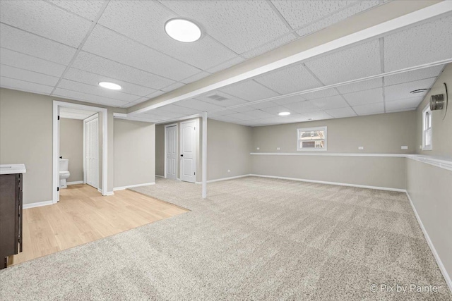 basement with a wealth of natural light, light carpet, and a drop ceiling