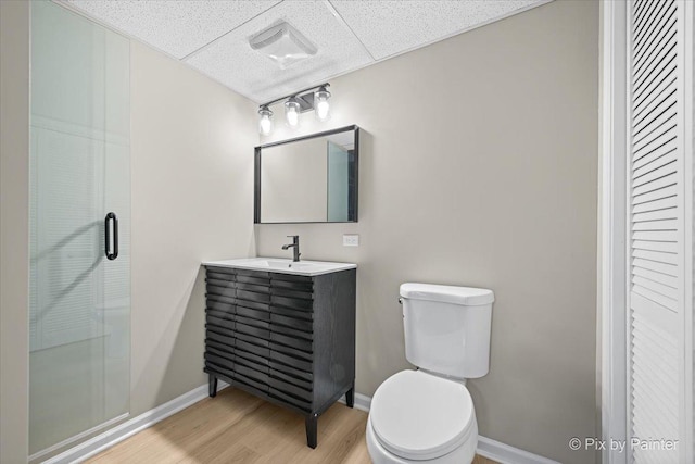 bathroom featuring hardwood / wood-style flooring, a paneled ceiling, vanity, a shower with shower door, and toilet