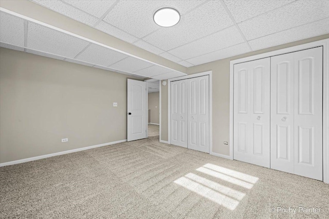 unfurnished bedroom featuring a paneled ceiling, carpet flooring, and two closets