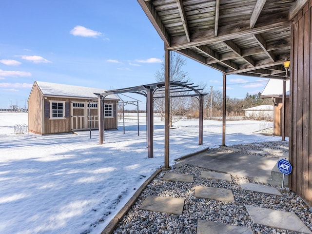 snow covered patio with a pergola and a shed