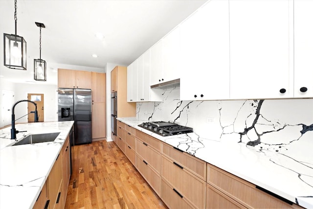 kitchen featuring appliances with stainless steel finishes, pendant lighting, sink, white cabinets, and light stone counters