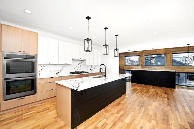 kitchen featuring a kitchen island with sink, hanging light fixtures, white cabinetry, and stainless steel double oven