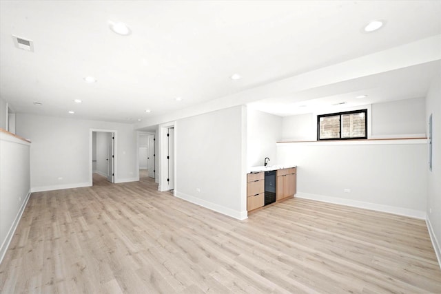 basement with bar, beverage cooler, and light hardwood / wood-style flooring