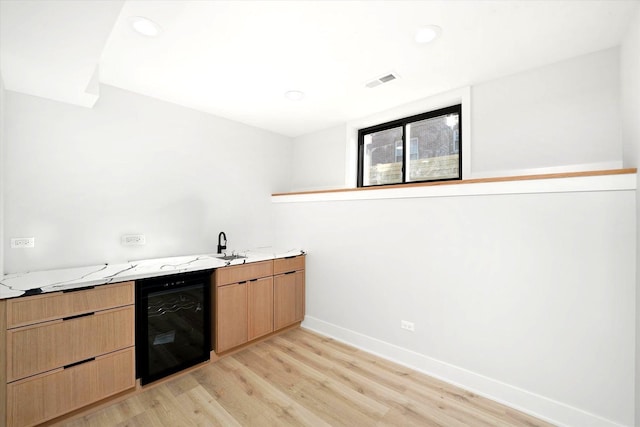 kitchen featuring light stone countertops, wine cooler, and light hardwood / wood-style floors