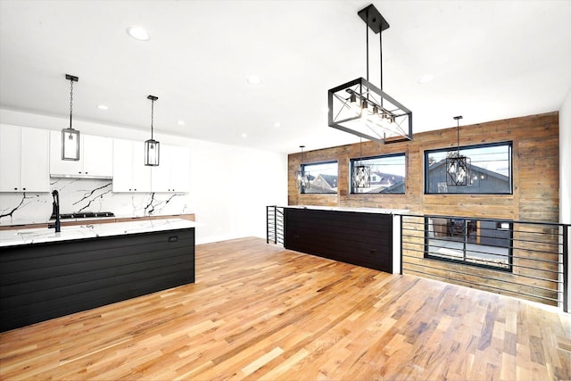 kitchen with wooden walls, decorative light fixtures, backsplash, white cabinets, and light hardwood / wood-style floors